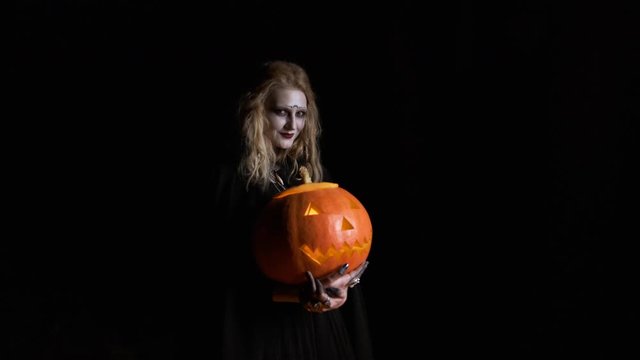 Halloween Image .Young Witch In Black Clothes Holds Pumpkin In Her Hands.