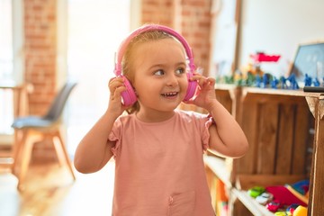 Beautiful blond toddler girl listening to music using headphones at kindergarten