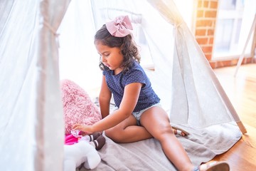 Beautiful toddler girl sitting on the floor playing with unicorn and doll inside  tipi at kindergarten © Krakenimages.com