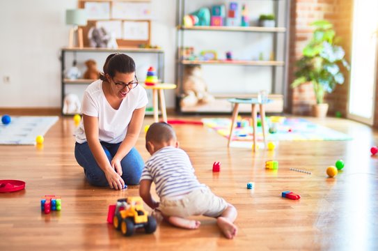 Beautiful teacher and toddler boy playing with tractor and cars at kindergarten