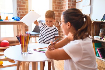 Beautiful teacher and toddler boy drawing draw using colored pencils at kindergarten