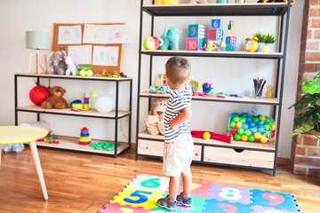 Beautiful toddler boy standing at kindergarten with lots of toys