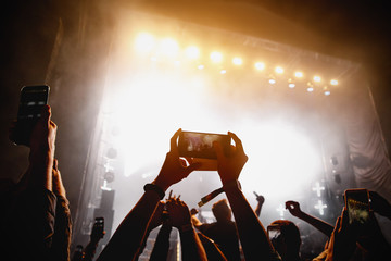 Crowd of people having fun while watching concert show at music festival. Raised hands with mobile...
