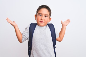 Beautiful student kid boy wearing backpack standing over isolated white background clueless and confused expression with arms and hands raised. Doubt concept.