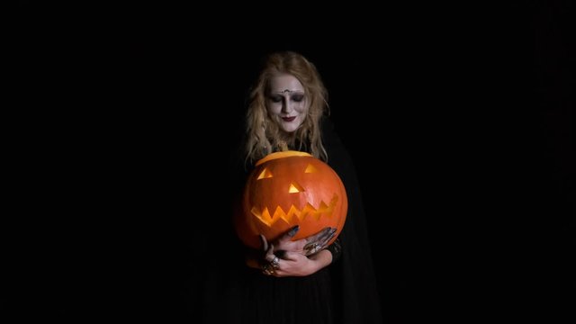 Halloween Image .Young Witch In Black Clothes Holds Pumpkin In Her Hands.