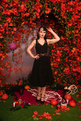 Slim fashion halloween girl with black hair in lace gothic pin up dress posing in the autumn background with fall leaves