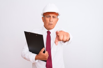 Senior architect man wearing security helmet holding clipboard over isolated white background pointing with finger to the camera and to you, hand sign, positive and confident gesture from the front