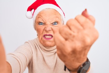 Grey-haired woman wearing Crhistmas Santa hat make selfie over isolated white background annoyed...