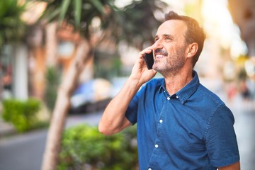 Middle age handsome businessman standing on the street talking on the smartphone smiling