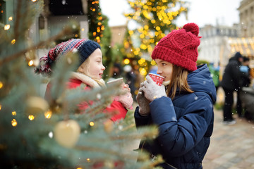 Two adorable sisters drinking hot chocolate on traditional Christmas fair in Riga, Latvia. Children enjoying sweets, candies and gingerbread on Xmas market.