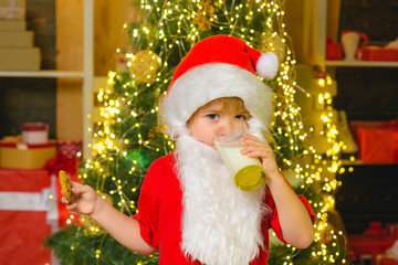 Fototapeta na wymiar Santa in home. Santa Claus eating cookies and drinking milk on Christmas Eve. Kid Santa Claus enjoying in served gingerbread cake and milk. Christmas for kid.