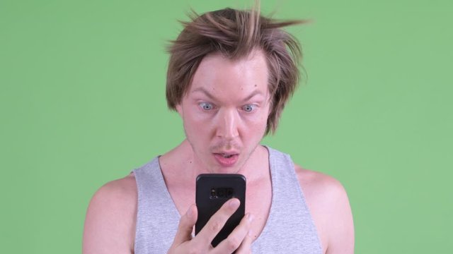Face of funny young man using phone and looking surprised with hair blown away