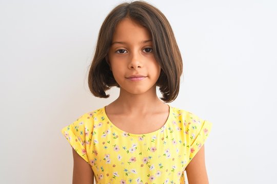 Young beautiful child girl wearing yellow floral dress standing over isolated white background with a confident expression on smart face thinking serious