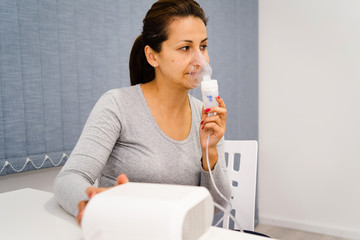 Portrait of adult woman using steam vapor inhaler nebulizer doing aerosol inhalation medicine...
