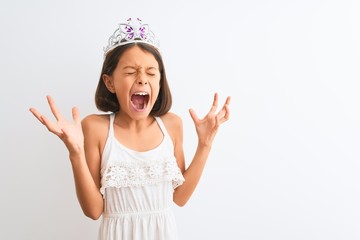 Beautiful child girl wearing princess crown standing over isolated white background celebrating mad...