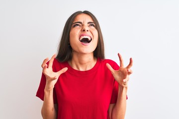 Young beautiful woman wearing red casual t-shirt standing over isolated white background crazy and mad shouting and yelling with aggressive expression and arms raised. Frustration concept.