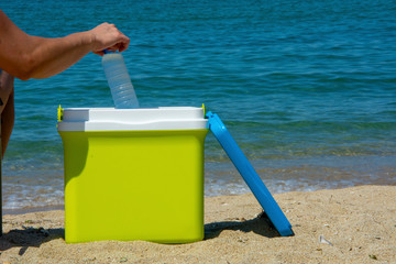 A human arm is taking a bottle of water from the portable refrigerator