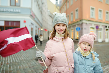 Two adorable little sisters celebrating Latvian Independence Day holding Latvia flag in Riga