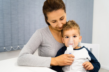 Woman mother hold her small son boy child using vapor steam inhaler nebulizer mask inhalation at...