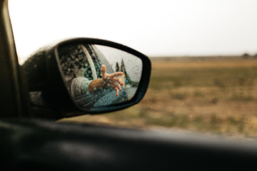 Hand touching rain drops. Mirror seen through the glass. Wet car window. Close up rain drop. Car view see the mirror. Rainy day.