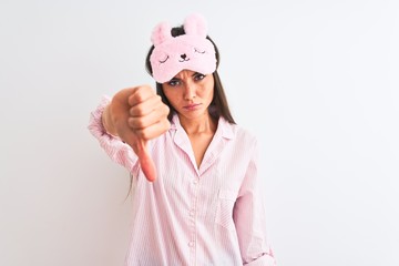 Young beautiful woman wearing sleep mask and pajama over isolated white background looking unhappy and angry showing rejection and negative with thumbs down gesture. Bad expression.