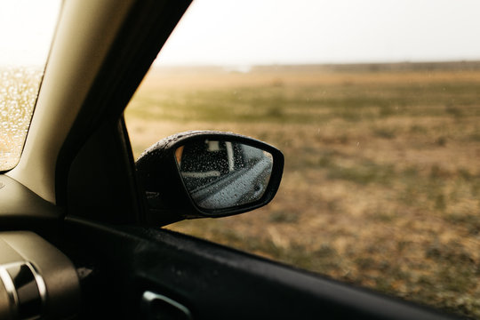 Rear view mirror seen through the glass. Wet car window. Close up rain drop. Car view see the mirror.