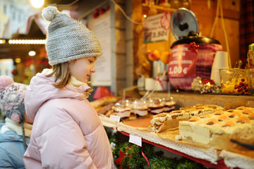 Cute young girl choosing sweets on traditional Christmas market in Riga, Latvia. Kid buying candy and cookies on Xmas.
