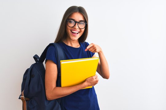 Young student woman wearing backpack glasses holding book over isolated white background very happy pointing with hand and finger