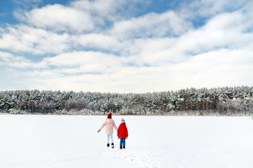 Two adorable young girls having fun together by beautiful frozen lake. Cute sisters playing in a snow.