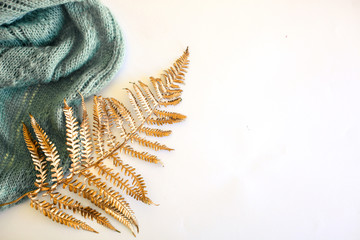 Leaf of golden trendy fern and blue knitted scarf against white background. Minimal flat lay, top view.
