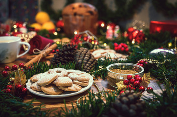 Fototapeta na wymiar Christmas ingredients table with a cookies in the center on a wooden board, accompanied by orange, panettone, cinnamon, pine. Festive pine decoration on red rustic background