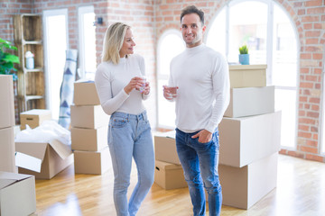 Fototapeta na wymiar Young beautiful couple standing drinking cup of coffee at new home around cardboard boxes