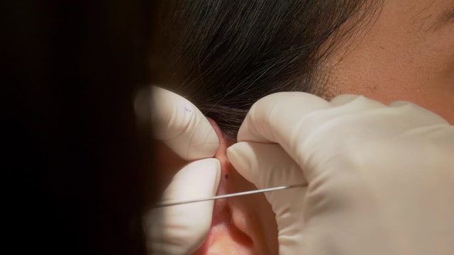 Woman gets pierced at the ear - piercing procedure in close up view