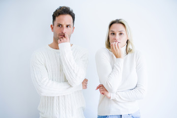 Young beautiful couple wearing casual t-shirt standing over isolated white background looking stressed and nervous with hands on mouth biting nails. Anxiety problem.