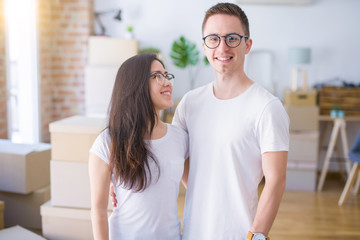Young beautiful couple wearing glasses standing at new home around cardboard boxes