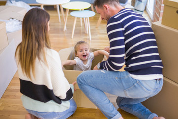 Beautiful famiily, kid playing with his parents riding cardboard fanny box at new home