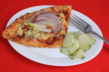 Closeup of large slice of vegetarian pizza with red onion on top and cucumber salad against red BG