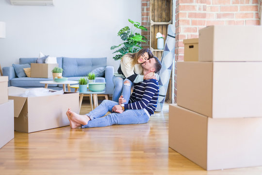 Young beautiful couple sitting on the floor at new home around cardboard boxes