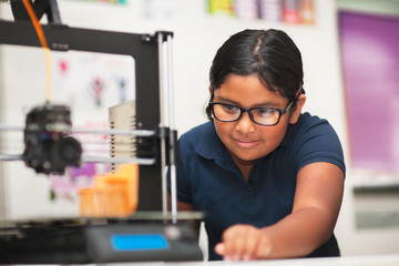 A female student in a modern classroom observing the printing process of a 3d model.