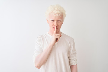 Young albino blond man wearing casual t-shirt standing over isolated white background asking to be quiet with finger on lips. Silence and secret concept.