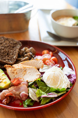 Substantial hotel breakfast with avocado and nuts, rye toasts, vegetables, fried bacon, chicken and poached egg