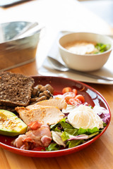 Substantial breakfast with avocado and nuts, rye toasts, vegetables, fried bacon, chicken and poached egg