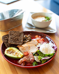 Substantial breakfast with avocado and nuts, rye toasts, vegetables, fried bacon, chicken and poached egg