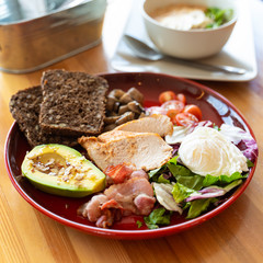 Substantial breakfast with avocado and nuts, rye toasts, vegetables, fried bacon, chicken and poached egg