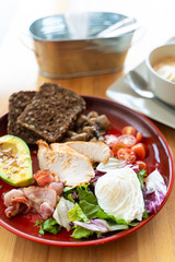 Substantial breakfast with avocado and nuts, rye toasts, vegetables, fried bacon, chicken and poached egg