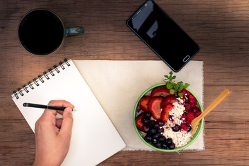 a hand writting in a notebook while having breakfast on a wooden rustic table