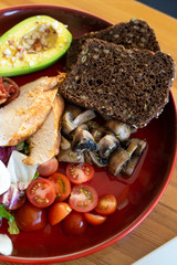 Close up of breakfast with avocado and nuts, rye toasts, vegetables, fried bacon, chicken and poached egg