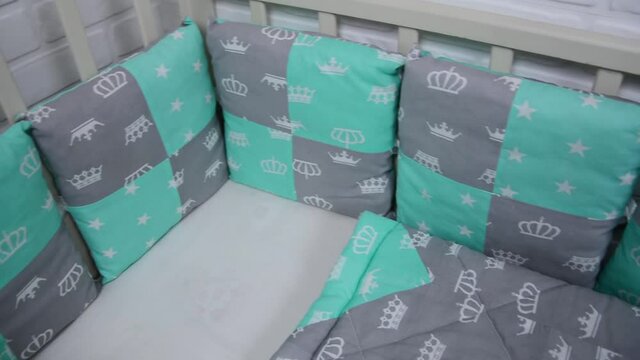 Baby bed linen in the baby's crib. The blanket, sheet, and pillows are green and gray with a pattern of crowns and stars.