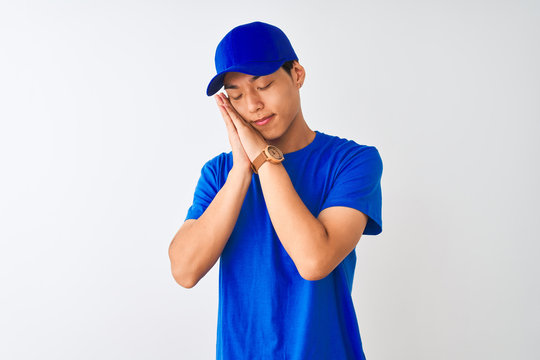 Chinese deliveryman wearing blue t-shirt and cap standing over isolated white background sleeping tired dreaming and posing with hands together while smiling with closed eyes.