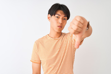 Young chinese man wearing casual striped t-shirt standing over isolated white background looking unhappy and angry showing rejection and negative with thumbs down gesture. Bad expression.